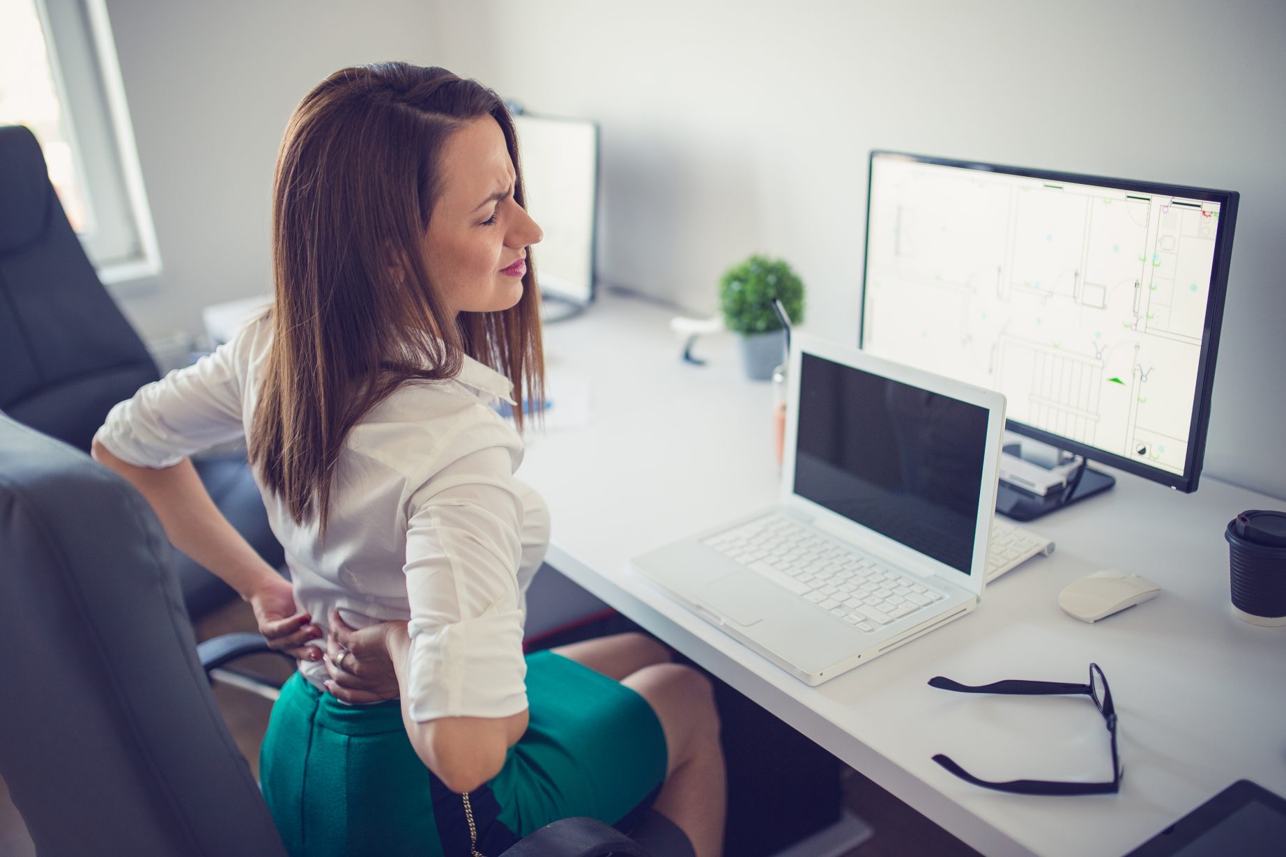 Young woman having back pain while sitting at desk in office